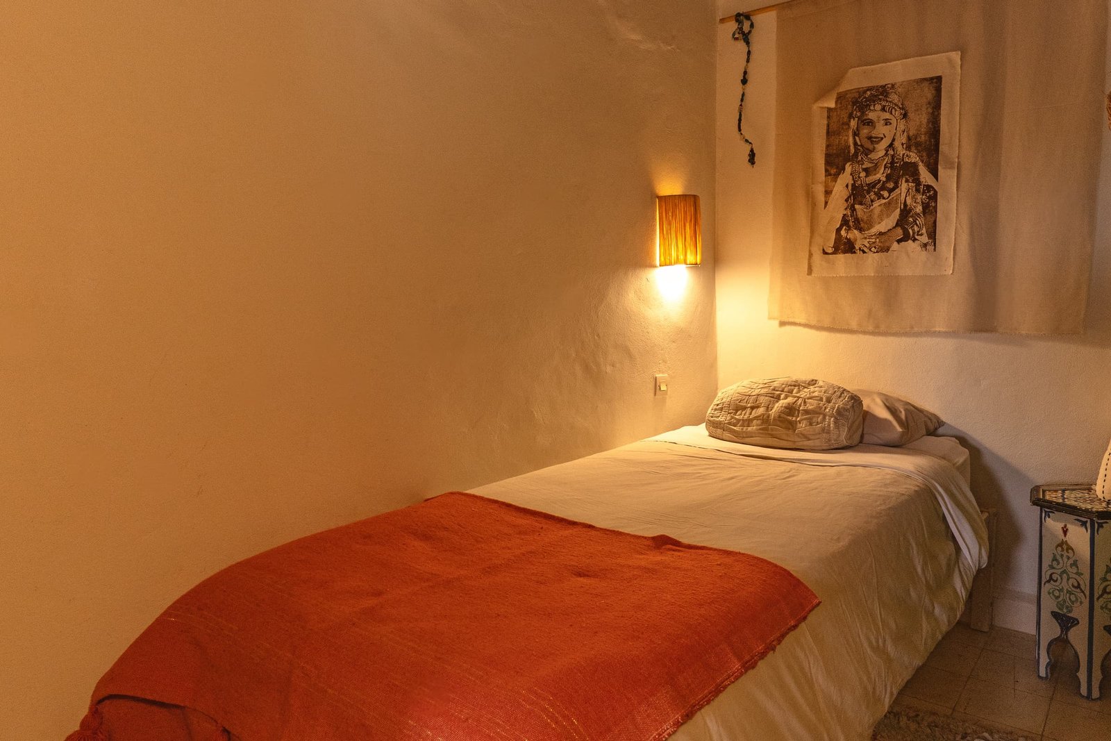 Un lit simple de la chambre Bohème, jeté orange et applique en cuivre