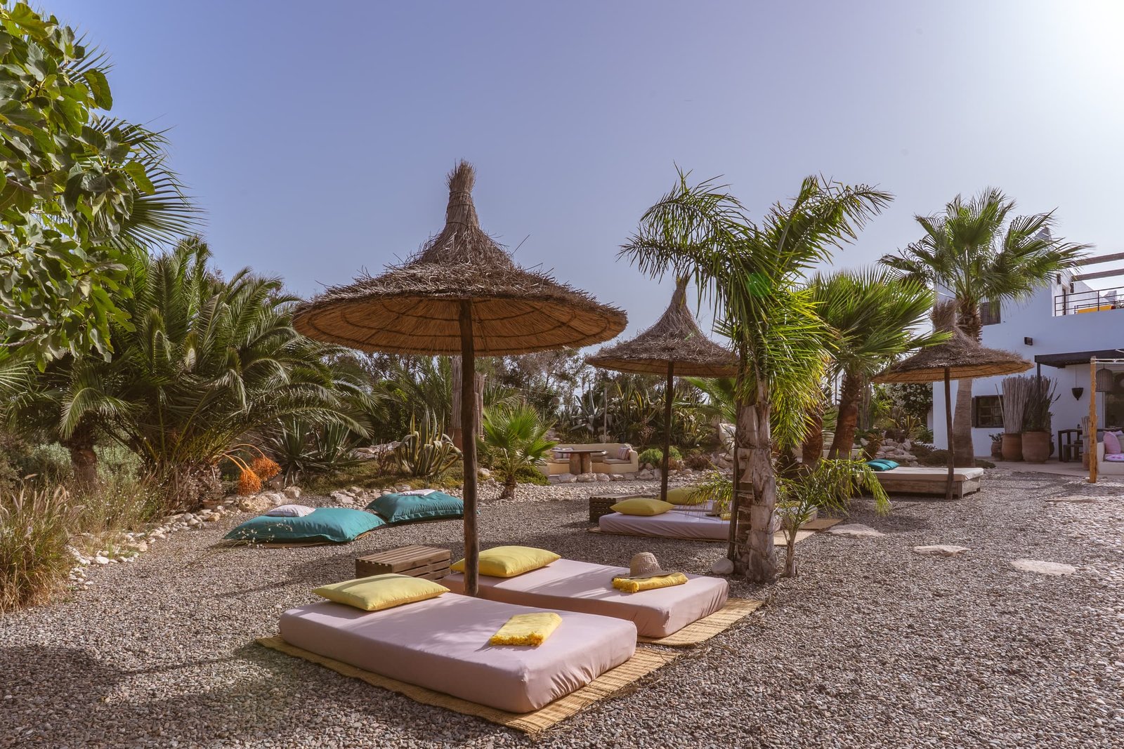 Deux parasols de paille et leurs bains de soleil, coussins turquoise sur les galets
