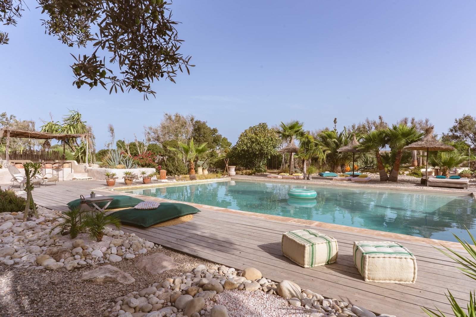 La terrasse en bois au bord de la piscine, ses poufs verts et ses galets
