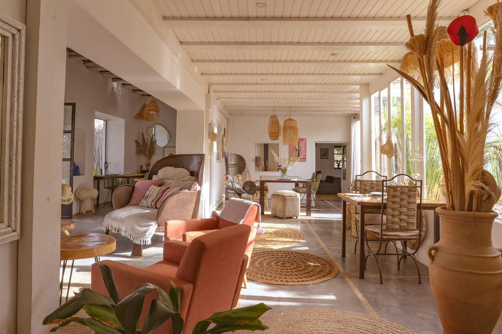 La véranda dans sa longueur, fauteuils corail et tapis ronds en jonc
