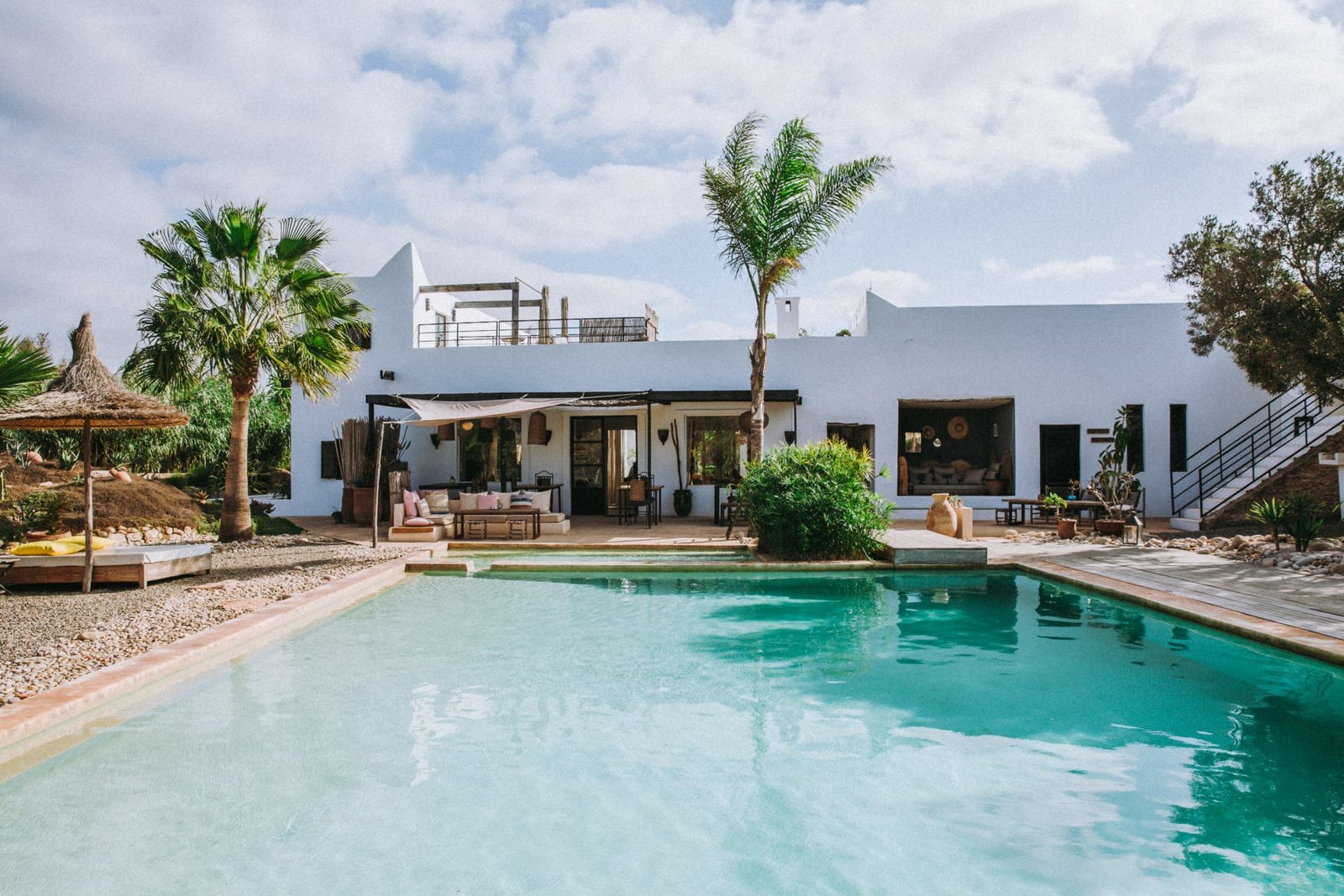 La piscine et la maison blanche entre les palmiers, en fin de matinée