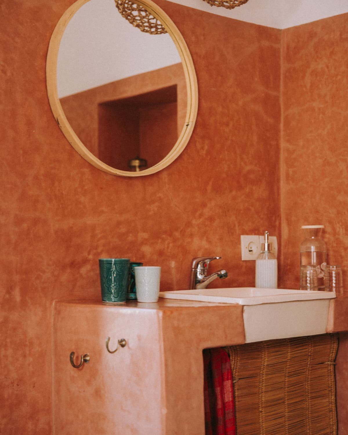 La salle de bain en tadelakt terre cuite, miroir rond et vasque blanche