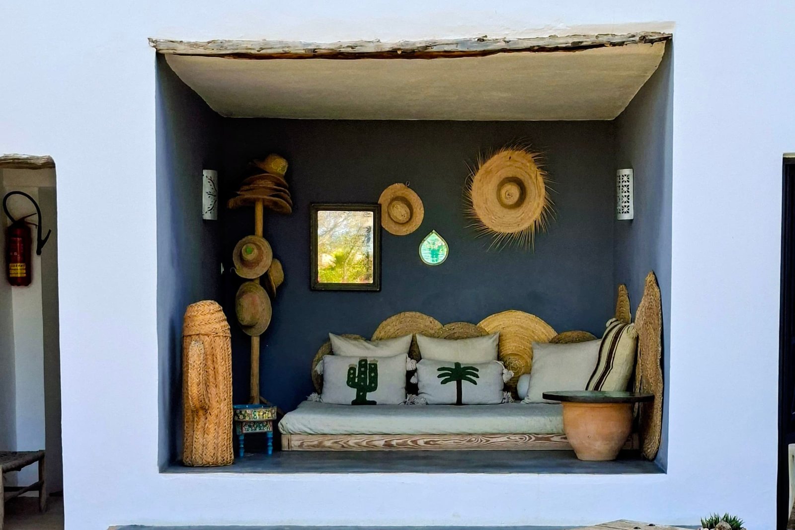 Alcove bleue avec sa banquette, chapeaux et paniers accroches au mur