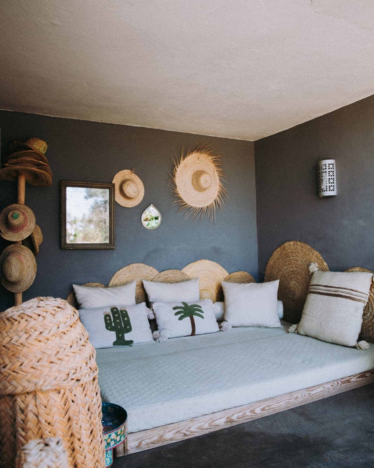 Banquette dans une alcove grise, chapeaux de paille et paniers au mur