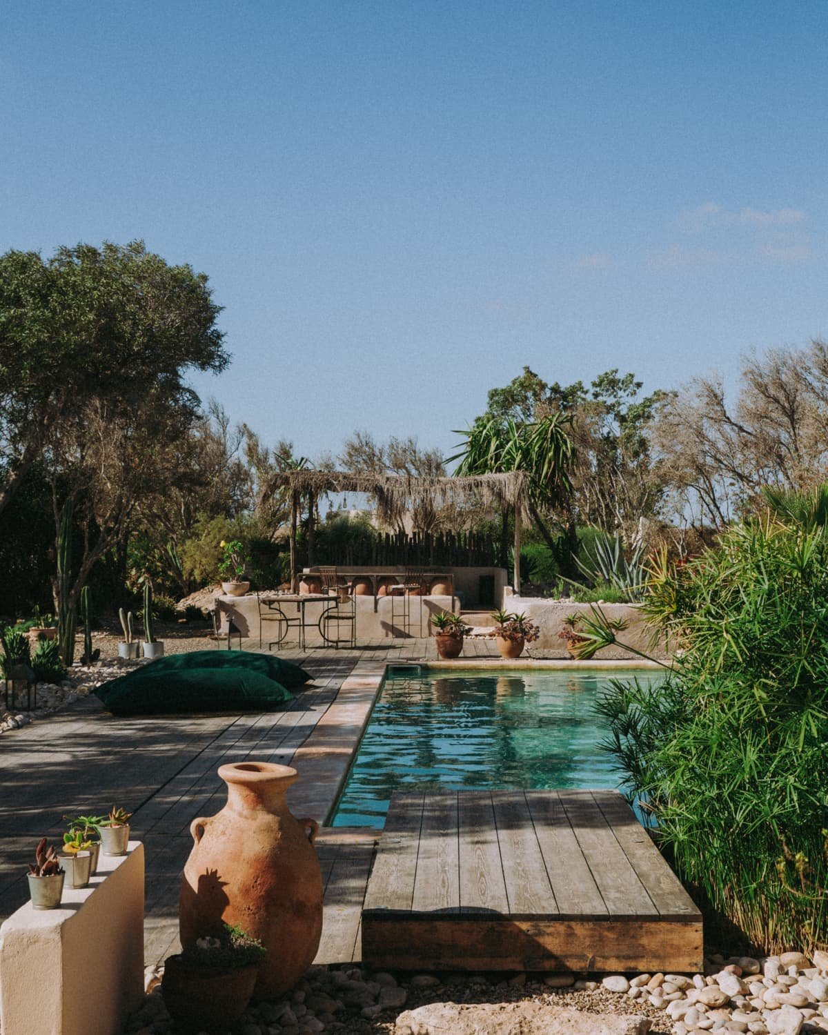 La piscine vue depuis la terrasse en bois, une jarre au premier plan
