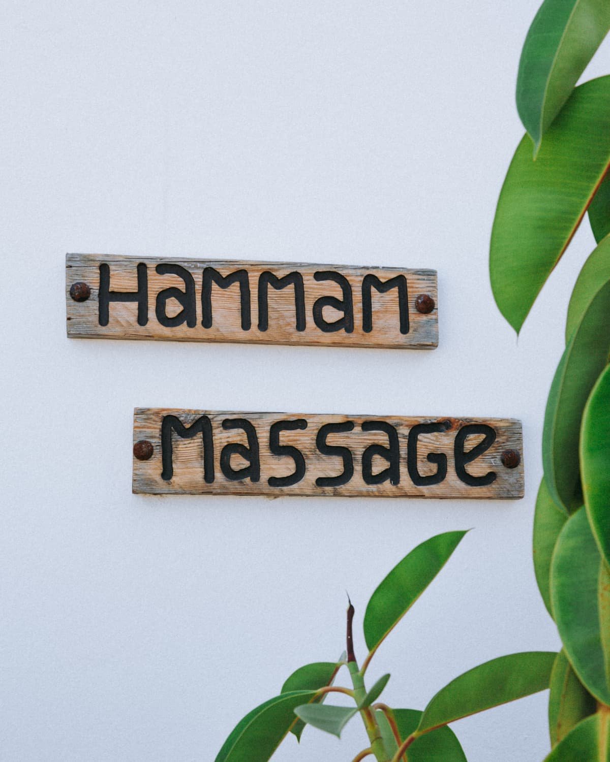 Deux planches de bois gravées, hammam et massage, sur un mur blanc