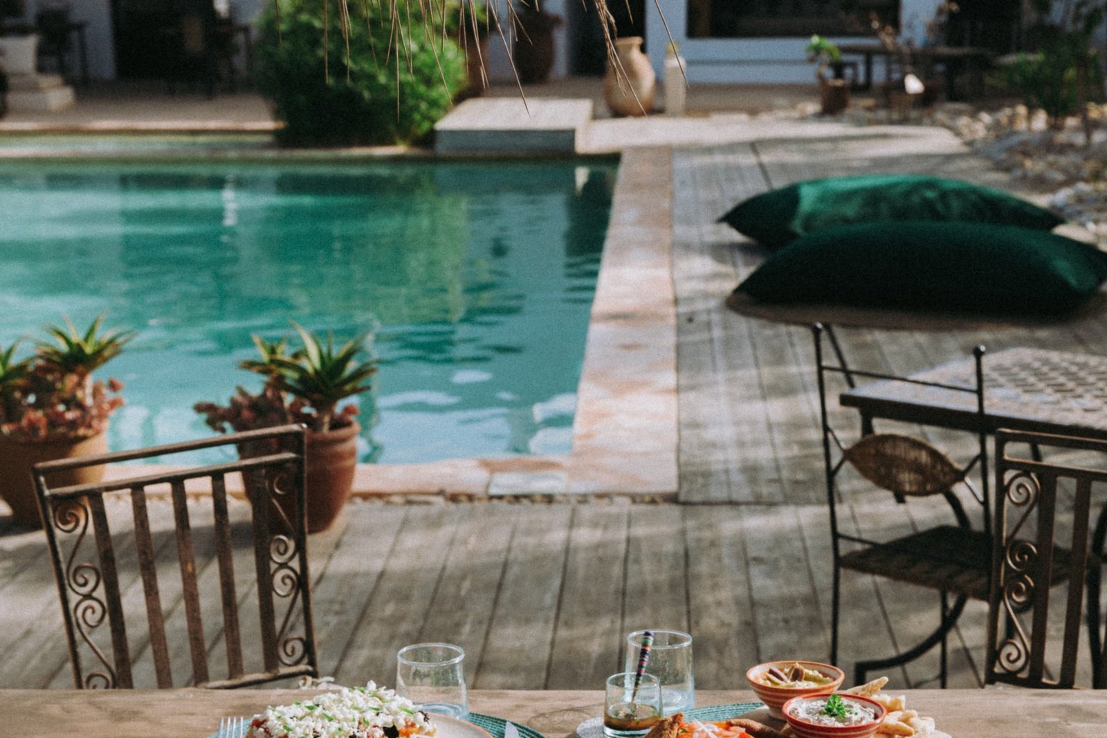 La table dressée au bord de la piscine, assiettes et carafe sur le bois